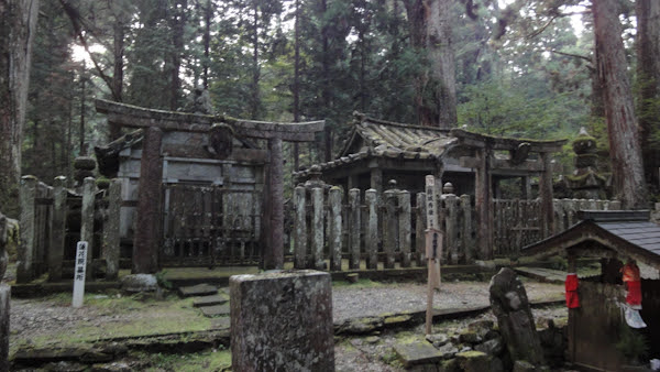 an old stone torii gate leads to a pair of old stone buildings fenced off by stone posts